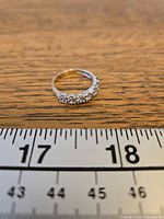 Ring lying flat showing seven stones and band profile beside ruler for scale