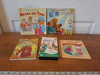 Five items spread on wood surface: four Berenstain Bears books and one VHS cassette