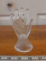 Front view of clear pressed glass hand ring holder next to ruler showing height