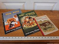 Three animal lithograph booklets laid out with ruler for scale