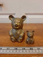 Front view of both brass bear figurines with ruler for scale