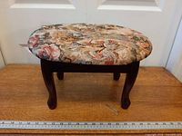 Side view of footstool showing wood legs and upholstered oval top