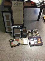 Photo showing multiple frames including tall inspirational framed text, multi-photo collage frames, and several small frames arranged on floor near table.