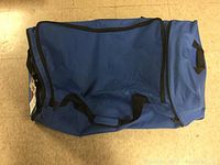 Blue duffel bag with black handles on floor, side view.
