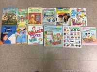 Photo showing 14 children's books arranged upright and flat on the floor. Titles include children's storybooks and activity books.