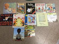 Photo showing 12 children's books arranged on a floor surface, titles visible and books in good condition with colorful covers.