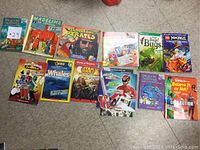 Books arranged in two rows on a floor, showing various children's book titles, colorful covers, and characters.