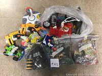 Photo showing a pile of assorted toys including building blocks, toy cars, a Nerf gun, and other small items in ziplock bags and clear plastic.