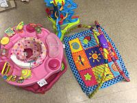 Top view of a pink baby activity center with toys, a multicolored fabric play mat with hanging toys, and a colorful ball track toy on the floor.