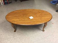 Full view of the oval wooden coffee table with polished surface and curved Queen Anne style legs.