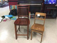 Pair of two wooden chairs pictured from the front on floor in room with other furniture and items.