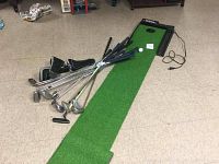 Full view of The Ultimate Putting System putting green with golf clubs on the floor nearby
