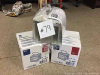 Photo of three metallic napkin dispensers wrapped in plastic resting on two boxes of Kimberly-Clark Professional napkins.