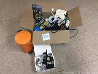 Wide view of box containing various electrical cords, adapters, phone handsets, wiring, and plastic items alongside a small orange container