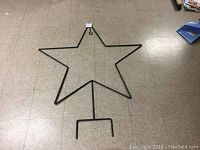Large metal star decoration on floor showing full outline and stake base.