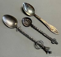 Three souvenir silver spoons laid out to show overall design