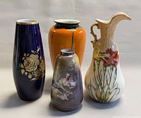 Group shot of four porcelain pieces: cobalt blue gold floral vase, orange vase, figural vase, floral ewer