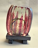 Front view of glass sculpture showing pink-red inclusions and multicolor loops on pedestal