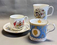 Front view of teacup on saucer with two commemorative mugs