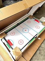 Opened carton showing air hockey surface with protective corner blocks