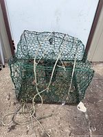 Front view of green wire-mesh crab trap showing overall form, attached rope, debris inside