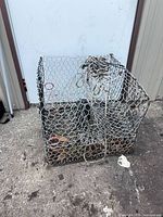 Front view of galvanized wire mesh crab trap with attached rope, rust visible on base