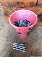Pink bucket containing many light blue pens, additional pens laid out in front