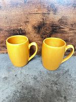 Front view of two yellow-orange mugs