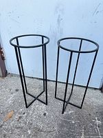 Two matching black metal plant stands on pavement