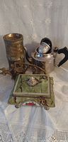 All three items grouped: brass trivet, metal teapot with infuser, footed English tea tin