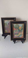 Both framed needlepoint artworks on stands, front view