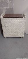 Front view of rectangular woven hamper with closed brown padded lid and handles