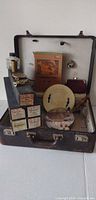Open suitcase showing all contents including piano roll boxes, book, plate, tray, coin purse, figurines