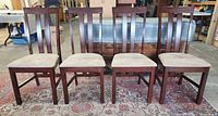 Front view of four matching brown wood chairs with beige seats