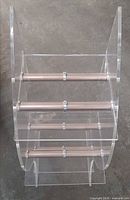 Front view of clear acrylic tiered stand showing three shelf levels and six metal rods