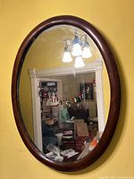 Front view of oval mirror mounted on wall, showing wood frame and reflective surface