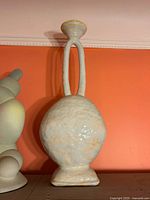 Full view of off-white ceramic vase with twin handles, bulbous body and pedestal base