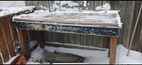 Front view of wooden workbench with plywood top, chicken-wire sides, snow covering surface