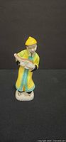 Front view of unmarked glazed porcelain Asian figurine in yellow robe holding scroll