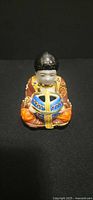 Front view of seated child figurine holding blue and gold bowl