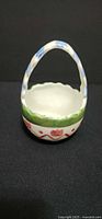 Front view of small glazed ceramic basket showing handle and painted design