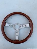 Front view of wood-rim steering wheel showing three brushed aluminum spokes