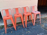 Front view of four orange metal counter stools against wall
