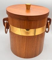 Front view showing teak body, gold band, lid with knob