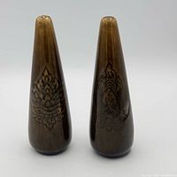 Front view of both ceramic shakers showing tapered form and lotus design