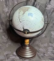 Front view of matte neutral world globe on metal ring and pedestal base