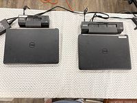 Two closed Dell Latitude E5440 laptops on their docking stations with AC adapters visible