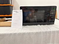 Microwave front view showing digital display and keypad, owner’s manual positioned beside unit