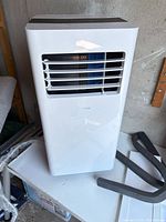 Front view of portable air conditioner showing louvered vent and accessories nearby