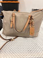 Front view of beige nylon crossbody bag with leather handles and strap